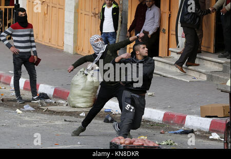 Dezember 11, 2017 - Hebron, West Bank, Palästina - palästinensische Demonstranten werfen Steine gegen israelische secrity Kräfte während der Auseinandersetzungen hinter einem Checkpoint im Zentrum der Stadt von der West Bank Stadt Hebron am 11. Dezember 2017, wie Demonstrationen weiterhin im Nahen Osten und anderswo über uns Präsident Donald Trump Erklärung von Jerusalem als Hauptstadt Israels zu Flare (Credit Bild: © Wisam Hashlamoun/APA Bilder über ZUMA Draht) Stockfoto