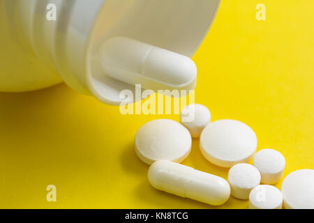 Haufen weiße Kapseln auf gelben Hintergrund. Die Pillen sind eine Linie oder Pfad. Konzept der Art und Weise, natürlich. Flasche auslaufen Tabletten. Stockfoto