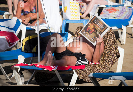 Mann liest Zeitung auf der Sonnenliege am Strand in Spanien Stockfoto