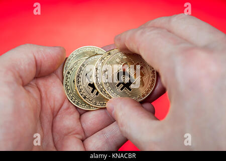 Die elektronische Währung bitcoin liegt in cash Münze in der Hand einer Person, eines roten Hintergrund. Stockfoto