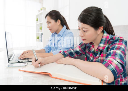 Hübsche attraktive Frau schreiben Hausaufgaben in Wohnzimmer und ihrer Klassenkameradin mit Mobile Laptop machen Schule Studium berichten. Stockfoto