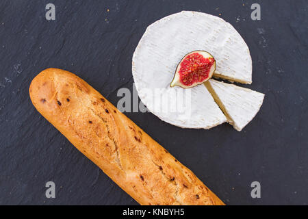 Helle saftige reife Stück Abb. Obst und cremige Schweizer Camembert Käse und einer knusprigen Golden frische Zwiebel Baguette zum Frühstück auf Graphit Hintergrund. Stockfoto