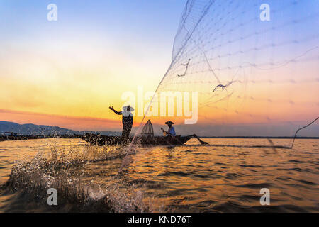 Silhouette der Fischer, die mit Netzen Fische am Bangpra See mit schönen Landschaften der Natur bei Sonnenaufgang zu verfangen. Stockfoto