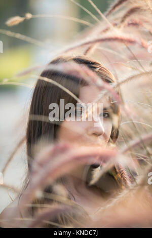 Ernsthafte junge Frau versteckt sich hinter den Pflanzen Stockfoto