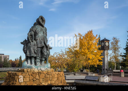 Unbekannte erste Familie Statue im goldenen Herzen Park in Fairbanks, Alaska, USA im Herbst zeigen Fairbanks Rotary 50-Uhr und Glockenspiel Stockfoto