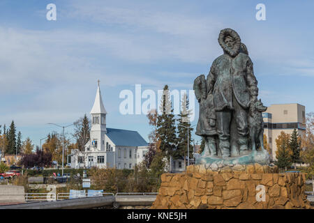 Unbekannte erste Familie Statue im goldenen Herzen Park in der Innenstadt von Fairbanks, Alaska, USA im Herbst mit der Unbefleckten Empfängnis Katholische Kirche Stockfoto