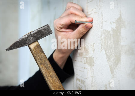 Hautnah auf einer Hand Hämmern einen Nagel an der Wand Stockfoto