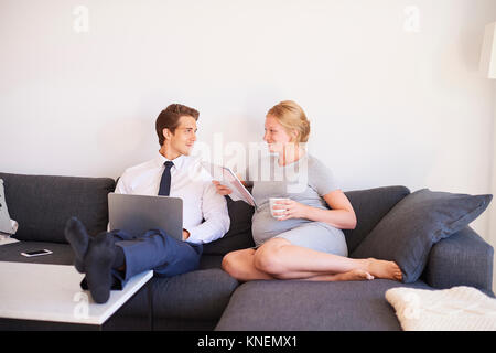 Schwangeren Paare sitzen auf einem Sofa mit Zeitschrift und Laptop Stockfoto