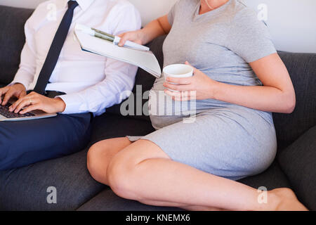 Hals nach unten an der schwangeren Paar sitzt auf einem Sofa mit Zeitschrift und Laptop Stockfoto