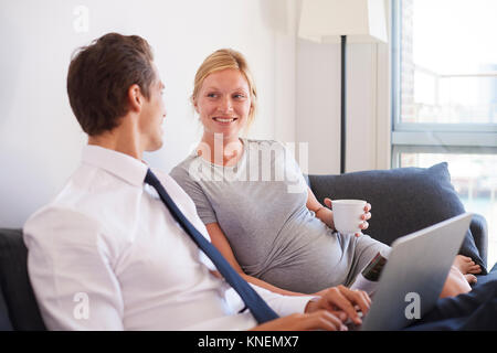 Schwangeren Paare sitzen auf einem Sofa Tippen auf Laptop Stockfoto