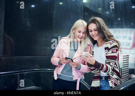 Zwei junge Frauen bewegen bis U-Bahnstation Rolltreppe am Smartphone suchen Stockfoto