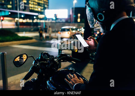 Reifen Geschäftsmann draußen in der Nacht, sitzen auf dem Motorrad, Motorrad Helm, tragen Sie ihr Smartphone, Rückansicht Stockfoto