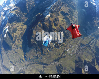 Luftaufnahme von zwei wingsuit Flyer, ein auf dem Rücken einer steht in roten Anzug oben Landschaft fliegen Stockfoto