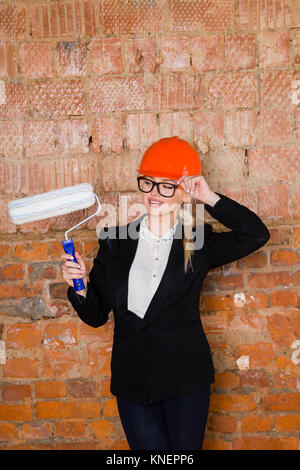 Porträt des Architekten student oder Maler mit farbroller und Schutz Helm tragen. Ziegelrot Hintergrund. Stockfoto