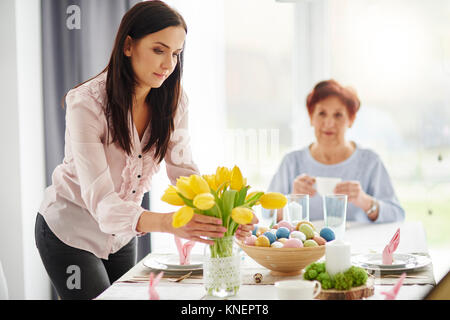 Mitte der erwachsenen Frau, die die gelbe Tulpen an Ostern Esstisch Stockfoto