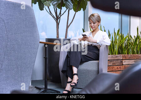 Geschäftsfrau, sitzen auf Stuhl im Büro mit Smartphone Stockfoto