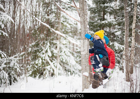 Mann hilft Sohn Baum Klettern in verschneiten Wald Stockfoto