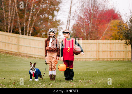 Portrait von Jungen, die Zwillingsschwester und Boston Terrier tragen Halloween Kostüme im Garten Stockfoto