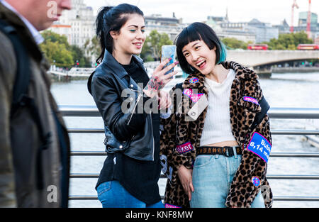 Zwei junge stilvolle Frauen am Millennium Fußgängerbrücke, London smartphone Lachen, Großbritannien Stockfoto