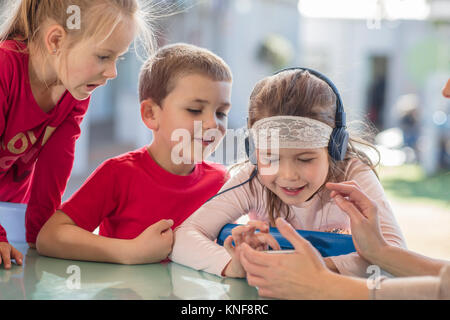 Junges Mädchen mit Freunden, mit Smartphone, das Tragen von Kopfhörern Stockfoto