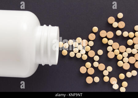 Gruppe der sortierten beige Tabletten. Kapseln verschütten aus weiße Flasche. Schwarzen Hintergrund. Stockfoto