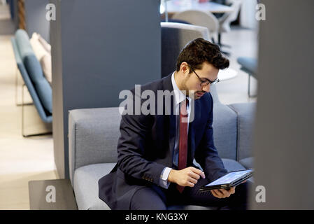 Latino Geschäftsmann in einem eleganten Anzug mit einem mobilen Tablet-Gerät in einem modernen Interieur gestaltet Amt bekleidet Stockfoto