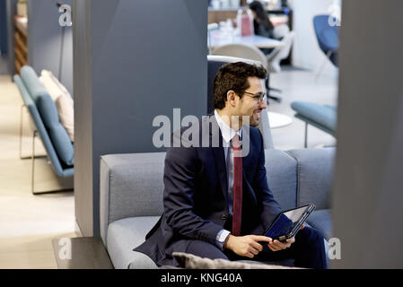 Latino Geschäftsmann in einem eleganten Anzug mit einem mobilen Tablet-Gerät in einem modernen Interieur gestaltet Amt bekleidet Stockfoto