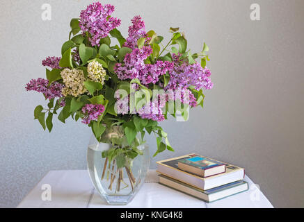 Auf dem Tisch steht eine Vase mit einem schönen Blumenstrauß Flieder in der Nähe sind Bücher. Stockfoto
