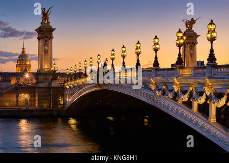 Pont Alexandre III Brücke und beleuchteten lampe Beiträge bei Sonnenuntergang mit Blick auf den Invalidendom. 7. Arrondissement, Paris, Frankreich Stockfoto