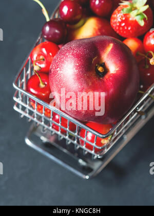 Frische rote Früchte und Beeren, Kirschen, Pfirsiche und Erdbeeren - im Supermarkt Warenkorb Fach auf schwarzem Hintergrund. Platz kopieren Stockfoto