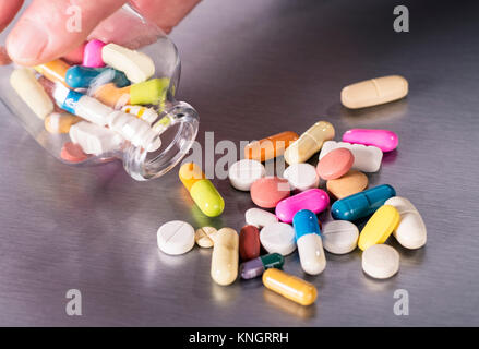 Viele verschiedene Tabletten sind von einem kleinen Glas Flasche auf eine metallene Fläche verstreut. Stockfoto