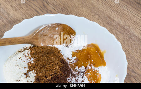 Stapel von Zutaten für die Zubereitung von süßen Weihnachten Lebkuchen. Detail von Mehl, Zucker, Honig und Gewürzen in Weiß dekorative Schale auf einem Holz Hintergrund. Stockfoto