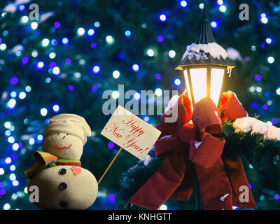 Schneemann Abbildung Holding ein Plakat mit Stock befestigt. Text "Frohes Neues Jahr!". Straßenlaterne in Red Ribbon und Tannenzweigen gewickelt. Stockfoto