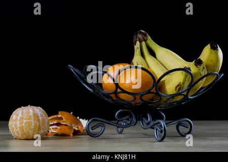 Leckere Früchte in einem Metallkorb. Drahtkorb mit Früchten auf einem Holztisch. Schwarzer Hintergrund Stockfoto