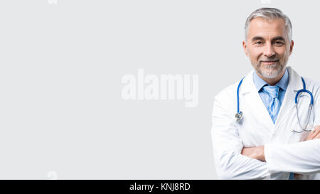Zuversichtlich reife Arzt posiert mit verschränkten Armen, er lächelt an Kamera Stockfoto