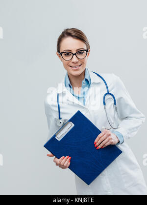 Selbstbewussten jungen Frau Doktor Lächeln und posieren mit Klemmbrett und Stethoskop Stockfoto