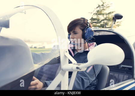 Lächeln Pilotin im Cockpit Leichtflugzeug, sie trägt Flieger Kopfhörer und Kontrollen überprüfen Stockfoto