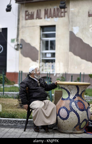 Ein bärtiger Mann mit einem traditionellen jellabiya sitzen neben einem großen Beton vase dekoriert mit einem Mosaik, in Alexandria, Ägypten, dargestellt am 02.11.2017. Ägyptens zweitgrößte Stadt, benannt nach Alexander dem Großen, erstreckt sich über 32 Kilometer entlang der Mittelmeerküste. Heute ist die Stadt gedacht wird, Heimat von rund 6 Millionen Menschen. | Verwendung weltweit Stockfoto