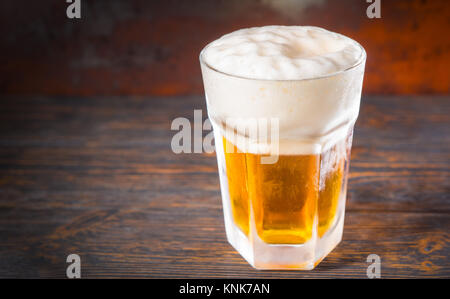 Grosse frozen Glas mit einem Bier und ein großer Kopf, der Schaum auf alten, dunklen Schreibtisch. Trinken und Getränke Konzept Stockfoto