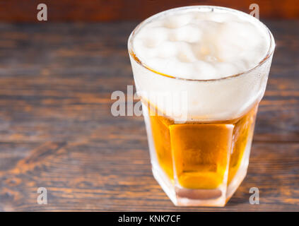 Blick von oben auf die großen Glas mit hellem Bier und ein großer Kopf, der Schaum auf alten, dunklen Schreibtisch. Trinken und Getränke Konzept Stockfoto