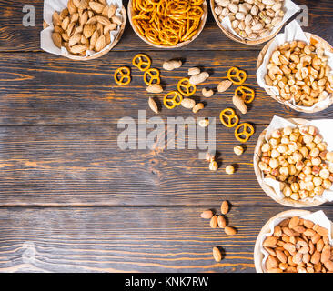 Blick von oben auf die verschiedenen Bier Snacks in Platten wie Pistazien, kleinen Brezeln und Erdnüsse auf dunklem Holzschreibtisch. Nahrungsmittel und Getränke Konzept Stockfoto