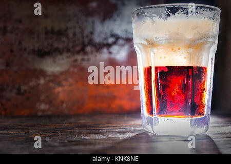 Grosse frozen Glas mit frisch gezapften Bier und rot Schaumkrone auf dunklem Holzschreibtisch. Nahrungsmittel und Getränke Konzept Stockfoto