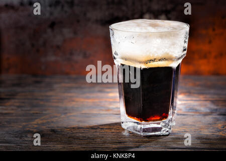 Grosses Glas mit frisch gezapften Bier und Leiter der Schaum auf Holzschreibtisch. Nahrungsmittel und Getränke Konzept Stockfoto