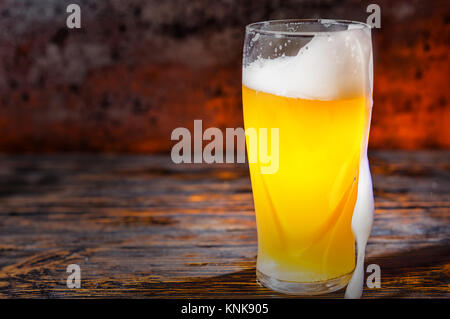 Grosse frozen Glas mit frisch gezapften Licht unfiltrierte Bier- und Überlauf Schaum auf dunklem Holzschreibtisch. Nahrungsmittel und Getränke Konzept Stockfoto