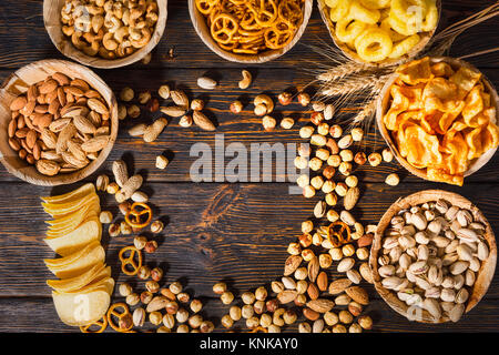 Blick von oben auf die Teller mit leckeren Bier Snacks in der Nähe von Weizen mit Kopie Raum im Zentrum auf dunklem Holzschreibtisch. Nahrungsmittel und Getränke Konzept Stockfoto