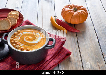 Pikante Kürbis creme Suppe mit Karotte und Chili Pfeffer, serviert mit Sahne und Croutons auf hölzernen Tisch. Zutaten: Kürbis, Karotten, Zwiebeln, Knoblauch, c Stockfoto