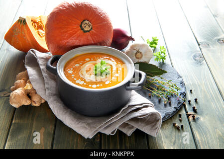 Kürbis creme Suppe mit Knoblauch, Zwiebel und Ingwer in Keramik Schüssel auf den Holztisch. Zutaten: Kürbis, Karotten, Ingwer, Zwiebeln, Knoblauch, Salz und Stockfoto