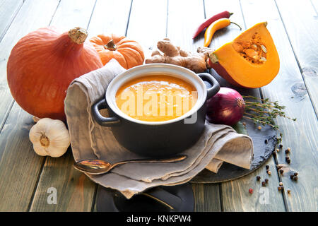 Pikante Kürbis creme Suppe, gewürzt mit Ingwer, Zwiebeln, Knoblauch und Chili, steht in Keramik Schüssel auf der Steinplatte auf dem hölzernen Tisch Stockfoto