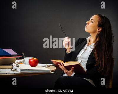 Foto von einem Lehrer oder Business Frau in den 30ern sitzen an einem Tisch vor einer großen Tafel denken. Stockfoto