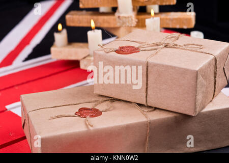 Boxen, eingewickelt in Handwerk Papier, mit packthread mit einem Wafer auf dem Hintergrund eines hölzernen Leuchter auf einem farbigen hölzernen Schreibtisch behoben. Stockfoto